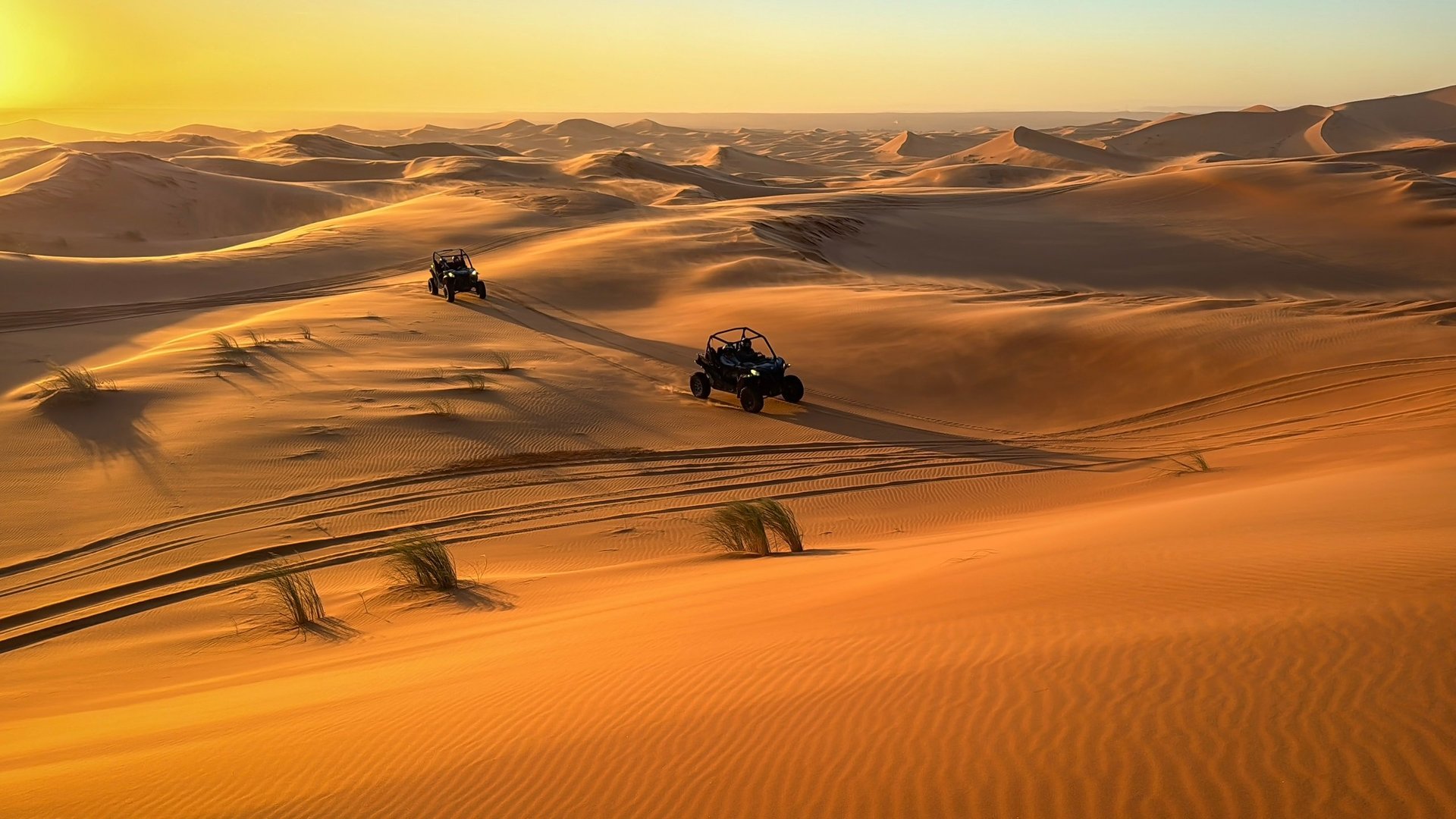 Two Polaris RZR buggies driving through red sand dunes at golden hour in the Dubai desert