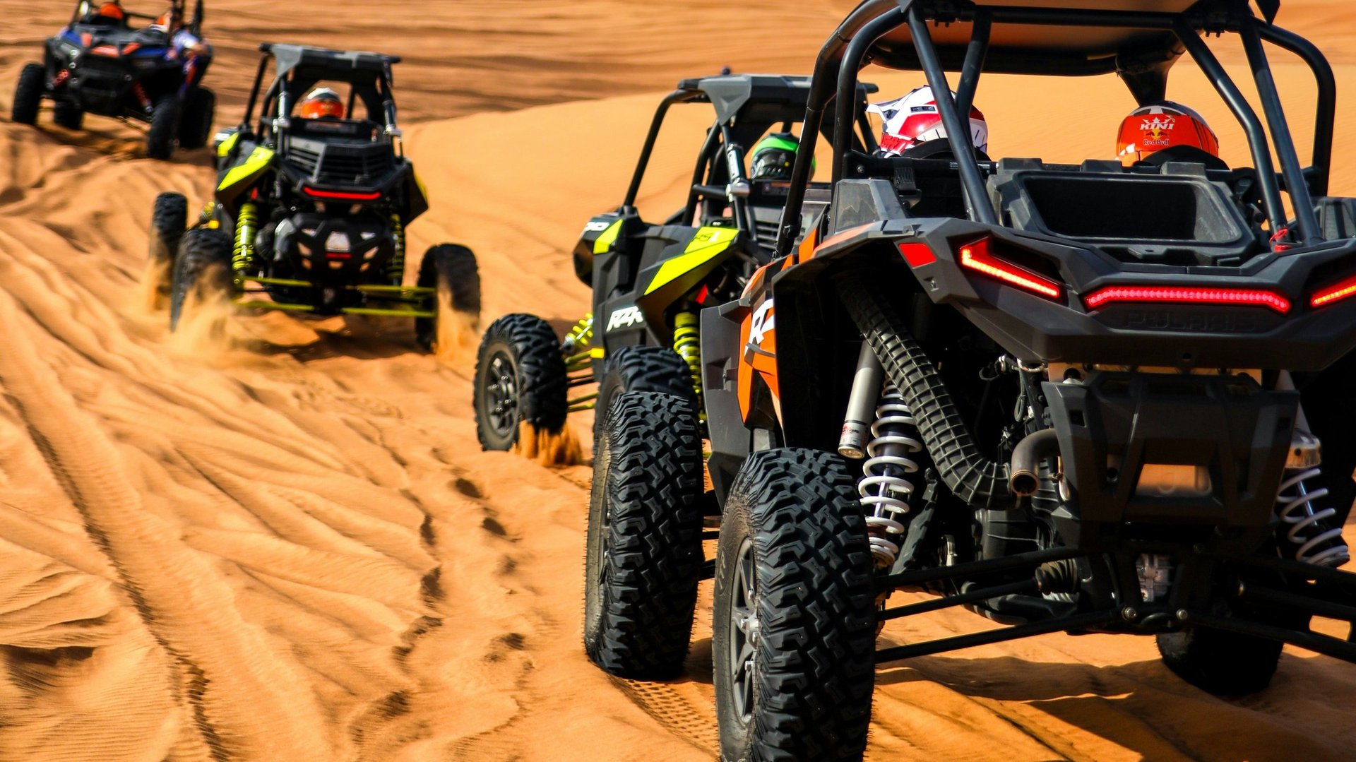 Three off-road buggies driving across sandy desert terrain with dunes in background